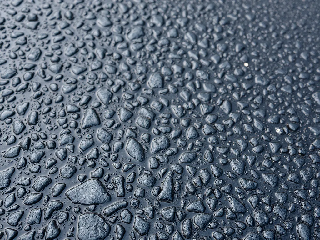 Close-up of water droplets on a waterproofed asphalt surface, showcasing the effectiveness of waterproofing methods.